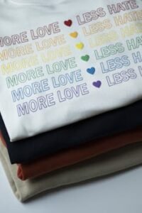 Stack of rainbow-themed shirts with 'More Love, Less Hate' message.
